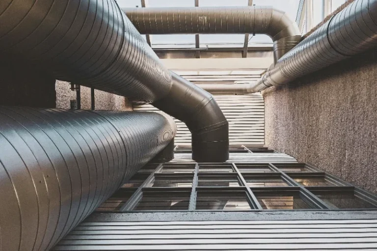 View of industrial pipes and structural framework from below, with natural light overhead.