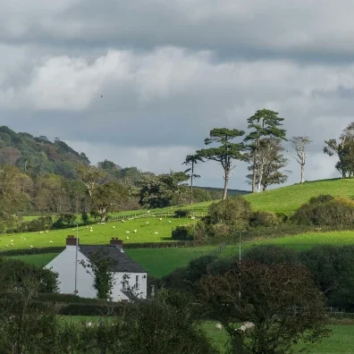 A white house surrounded by lush green fields and trees under a cloudy sky.