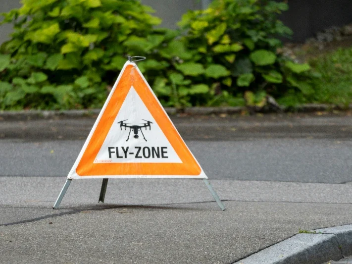 Warning sign indicating a drone fly zone, displayed on a triangular orange background.