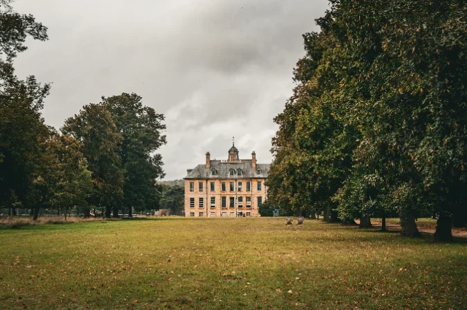 Stately home grounds A grand building surrounded by trees and a grassy area under a cloudy sky.