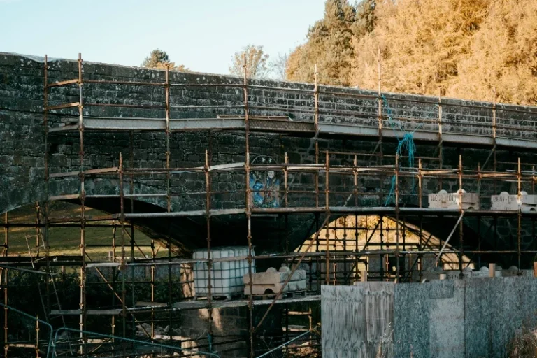 Bridge with scaffold around Construction work on a stone arch bridge, surrounded by scaffolding and materials.