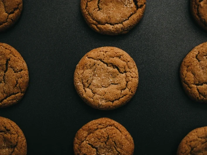 Chocolate chip cookie with a bite taken out, surrounded by crumbs on a light background.