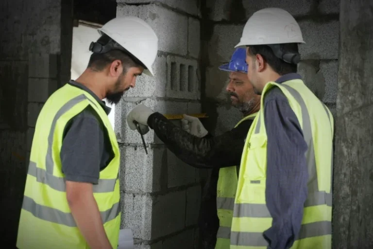 Workers checking work Three construction workers in safety vests and helmets collaborating on a building project.