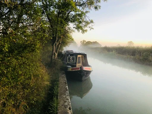 Narrow-boat-for-sale Narrowboat moored on a misty canal surrounded by lush greenery.