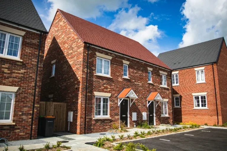 New build houses Two red-brick houses with pitched roofs, set in a landscaped area under a blue sky.